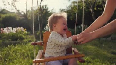 Happy Children's Day. Mother having fun with her happy baby on a swing. Slow motion. Sunny playground in the backyard. Concept of autism.