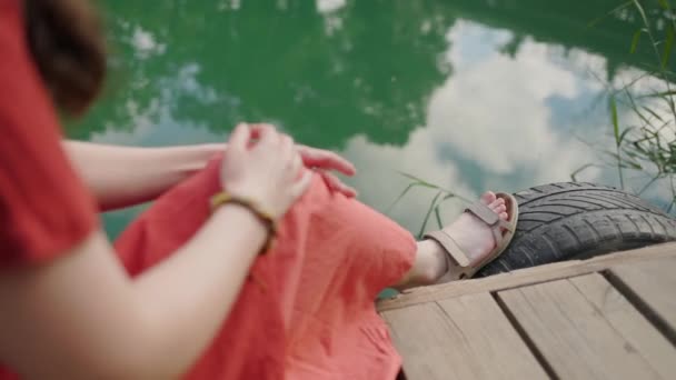 Woman Red Dress Sits Wooden Dock Adjusts Her Clothes Hands — Wideo stockowe