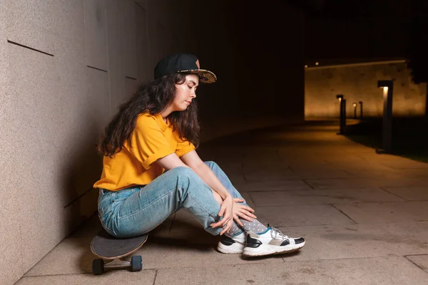 若い女性はスケートボードに座って 夜の通りにポーズをとっています 屋外だ サイドビュー 若者サブカルチャーの概念 — ストック写真