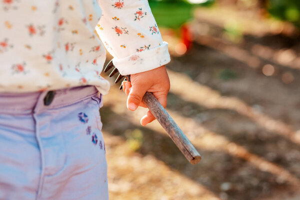 Маленький ребенок держит в руке грабли для игрушек. Рука крупным планом. Концепция садоводства и Дня Земли.