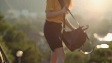 Yaz zamanı. Yürüyen kadın oturur, sırt çantasını çıkarır ve şapkasıyla kendini yelpazeler. Şehir çok sıcak. Arkadan bak. Gerçek zamanlı..