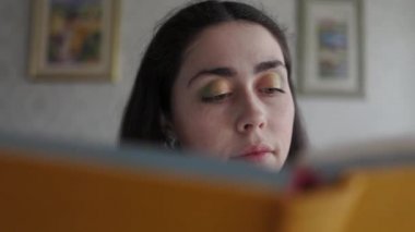 Genç bir kadın bir kitap okuyor, kaldırıyor, ve akıllı telefonunu çıkarıyor, yazarken gülümsüyor. Kamerayı aşağı çek. Çevrimiçi bağımlılık kavramı.