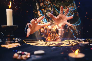 Cadı tarot kartlarını masaya yaymış ve piramidin üzerinden okuyordu. Eller yakın çekim. Kehanet ve astroloji kavramı.