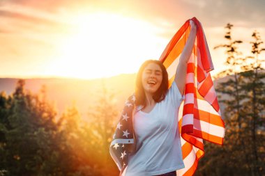 Bağımsızlık Günü. Kafkasyalı mutlu genç bir kadın elinde bir Amerikan bayrağı salladı. Arka planda gün batımı. Amerikan Ulusal Tatil Konsepti.