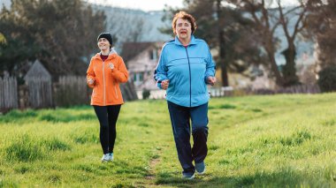 Kafkasyalı büyükanne ve torunu birlikte koşuyor. Spor kıyafetleri içinde yaşlı ve genç kadınlar parkta koşuyor. Uluslararası Yaşlılar Günü 'nde. Sağlıklı yaşam tarzı ve spor kavramı.