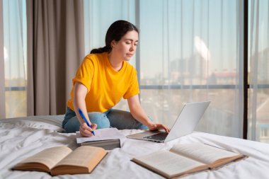 Online eğitim. Beyaz bir kadın bir yatakta oturuyor ve bir dizüstü bilgisayar üzerinde çalışıyor. Çevrimiçi kurslar ve uzak çalışma kavramı.