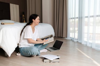 Genç bir öğrenci yerde oturuyor ve elinde bir kitap tutuyor, gülüyor. Uzayı kopyala Online kurslar ve eğitim kavramı.