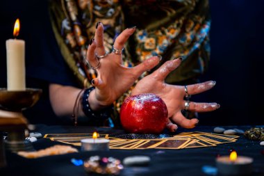 Bir falcı, Tarot kartlarının üzerinde duran kırmızı bir elmayı ortaya çıkarır. Masanın üzerinde yanan bir mum ve muska var. Kapatın. Kehanet, astroloji ve ezoterizm kavramı..