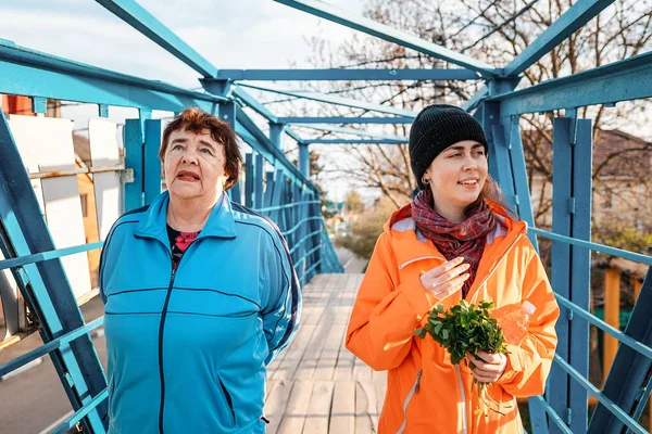 Grandmother and adult granddaughter walk together on the bridge. Family Outdoor walk. The concept of the International Day of Older Persons.