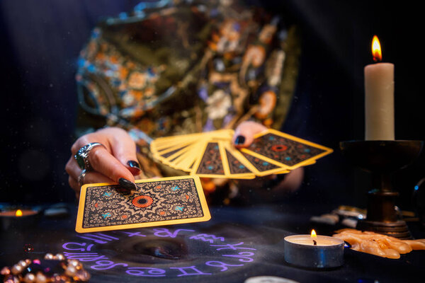 Предсказательница держит в руках фаната карт и протягивает карту одной рукой. Астрологический круг светится под рукой. Крупный план. Понятие гадания, магии и эзотерики.