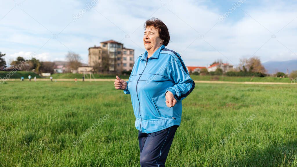 Running and sports activity. Portrait of mature smiling grandmother in sports clothes runs through a green field. The concept of the International Day of Older Persons.