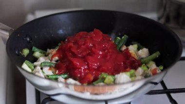 Bir kadın tavada Tayland yemeği pişiriyor. Domates ve karışım ekliyor. Gerçek zamanlı. Kapat..