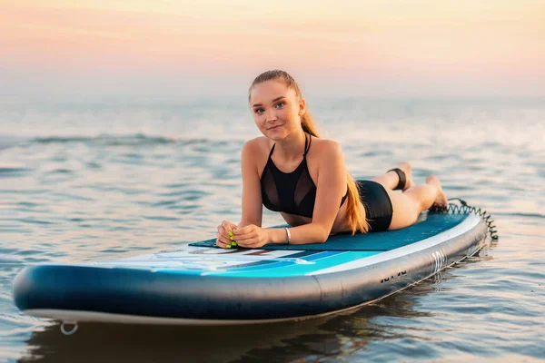 非常健康的女孩躺在海面上的一块冲浪板上 在背景中 海洋和日落 夏季活动和极端娱乐活动 — 图库照片