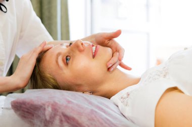 Tıp ve kozmetoloji kavramı. Genç bir kadın akupunktur yüz masajı seansında, yakın plan. Yan görünüm.