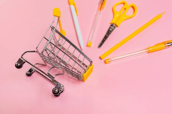 回到学校和购物的概念 粉色背景的黄色办公用品玩具购物车 — 图库照片
