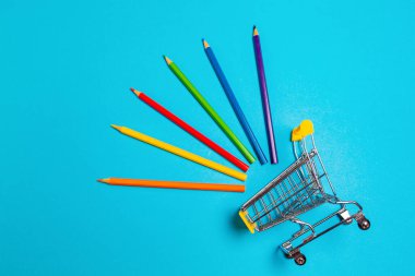 Mavi arka planda renkli pastel boyalı bir alışveriş arabası. Düz yatıyordu. Okula dönüş kavramı.