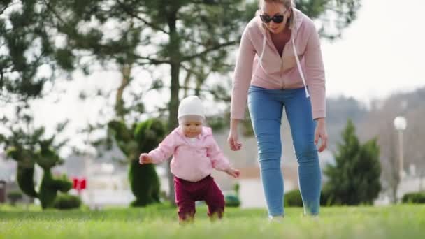 白人の母親は赤ん坊に歩くことを教える 母親と子供が公園を歩いている リアルタイムだ スローモーション 子供の発達の概念 — ストック動画