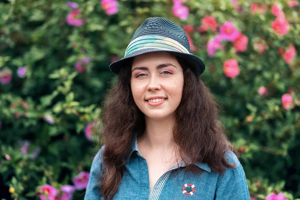 花の茂みの背景にわらの帽子に笑みを浮かべて美しい若い女性の肖像画 3月8日と母の日の概念 — ストック写真