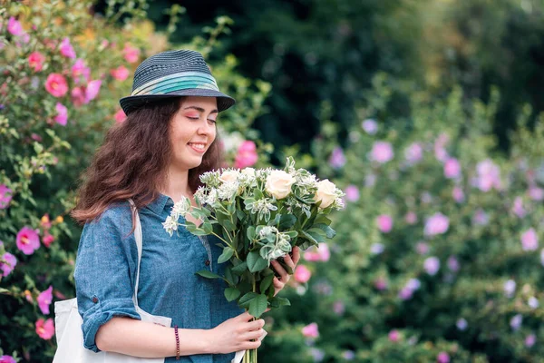一个戴着草帽 手持一束白玫瑰的年轻快乐女人的画像 背景上的花丛 三月八日和母亲节的概念 — 图库照片
