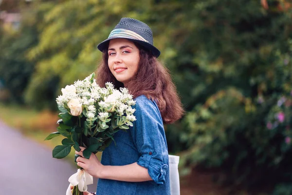 一个戴着草帽 手持一束白玫瑰的年轻漂亮女子的画像 背景上的植物和树木 三月八日和母亲节的概念 — 图库照片