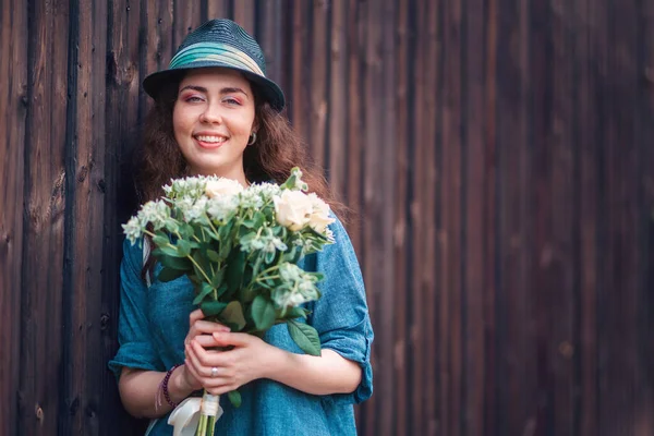 木製のフェンスの背景に白いバラの花束を保持藁帽子の若い美しい女性の肖像画 3月8日と母の日の概念 — ストック写真