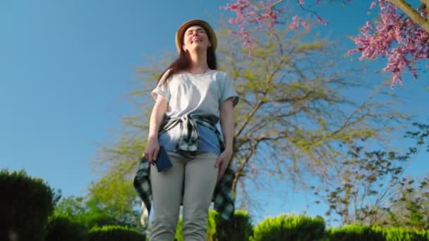 Eine Lächelnde Hübsche Frau Mit Strohhut Steht Unter Einem Sakura — Stockvideo