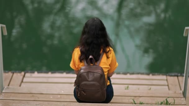 Young Woman Sitting Pier Bank River Throws Pebble Water Camera — 图库视频影像