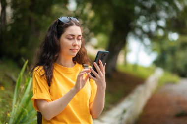 Akıllı telefondan yazı yazan hoş bir kadının portresi. Video iletişim konsepti. Arka planda tropikal park.