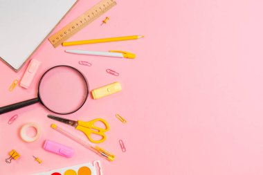 Pembe arka planda büyüteç, defter ve sarı ofis malzemeleriyle kompozisyon. Düz yatıyordu. Uzayı kopyala Eğitim kavramı ve okula dönüş.