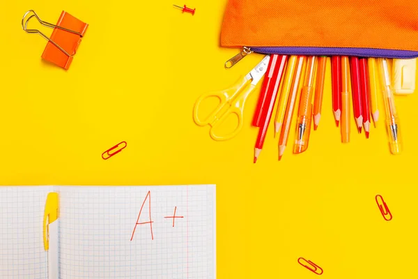 Education. Pencil box with pens and notebook with an excellent grade on a yellow background with clips. Flat lay. Concept of back to school.