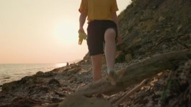 Okyanus kıyısını temizliyorum. Kirli bir plajda lastik eldiven takmış bir kadın gönüllü yürüyor. Eller yakın çekim. Dünya Günü konsepti.