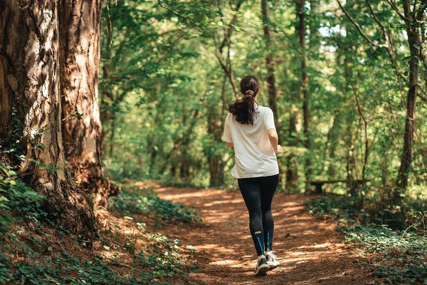 Cross-country running. A young woman in sports clothes is jogging in the morning summer forest. Back view. Concept of outdoor training.
