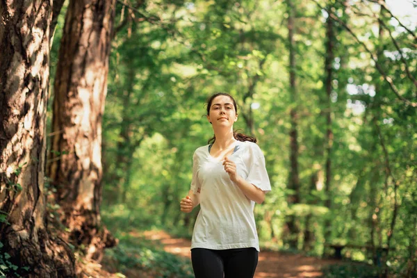 Portrait of young woman in sports clothes is jogging at summer forest. The concept of cross-country running and wellness.