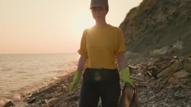 Bir kadın gönüllü plajda plastik bir torba içinde plastik şişe topluyor. Gerçek zamanlı. Dünya Günü ve çevresel koruma kavramı.