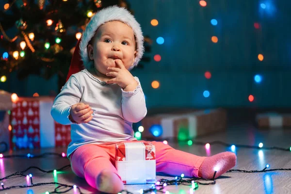 Wintervakantie Verrast Baby Meisje Een Kerstmuts Zittend Met Feestelijke Lichtjes — Stockfoto