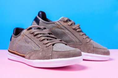 Bir adamın gri tuvalden yapılmış, pembe-mavi arka planda duran yeni spor ayakkabıları. Kapat..