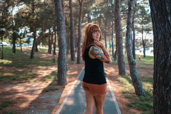 Кавказская Молодая Улыбающаяся Женщина Татуировкой Руке Гуляет Летнем Парке Оборачивается — стоковое фото