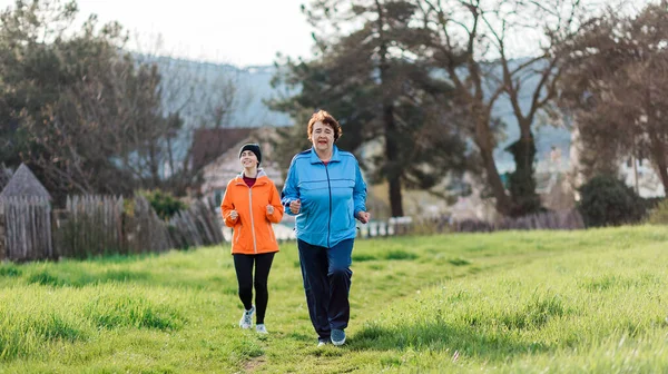 The concept of a healthy lifestyle and sports. Elderly and young women in sports clothes, running in the park. Grandmother and granddaughter run together. International Day of Older Persons.