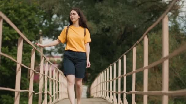Μια Νεαρή Χαμογελαστή Λευκή Γυναίκα Περπατάει Στο Πάρκο Στη Γέφυρα — Αρχείο Βίντεο