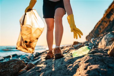 Dünya çevresi günü. Bir aktivist plajdan plastik bir şişe aldı. Kapatın. Arka planda, deniz ve günbatımı. Alt manzara. Kıyı bölgesini temizleme kavramı.