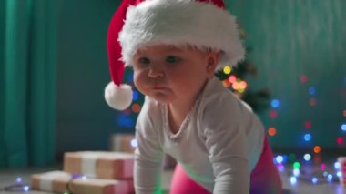 Noel şapkalı tatlı bir kız, festival ışıklarında sürünüyor. Ağır çekim. Noel tatili konsepti.