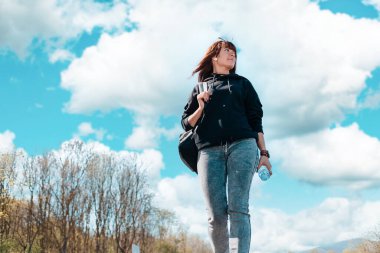 Genç ve güzel bir kadın elinde sırt çantasıyla yürüyor. Alt manzara. Uzayı kopyala Otostop ve yerel seyahat kavramı.