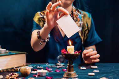 Kehanet ve astroloji. Cadı elinde boş bir beyaz tarot kartı tutuyor ve mumları yakıyor. Model yap. Uzayı kopyala Haritacılık ve falcılık konsepti.