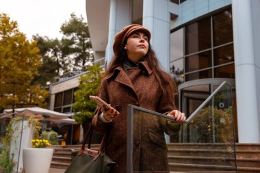 Genç bir kadın akıllı telefonunu tutarak ve sonbaharı kucaklayarak tek başına yürürken şehirde zarif bir hareket. Alt görünüm.