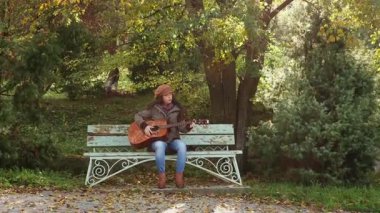 Güzel, genç, beyaz bir kadın parkta gitar çalıyor. Geniş açı. Müzik aletleri çalmayı öğrenmek.