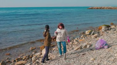 İki gönüllü kadın, kirlilikle savaşmak ve çevreyi korumak için vahşi sahilden çöp topluyor. Kadınlar bir fren yapar ve çay içerler. Okyanus temizliği kavramı. Geniş açı.