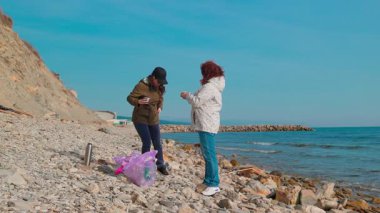 Gönüllüler, yaban hayatını korumak ve sahilin doğal güzelliğini geri kazanmak için sahil boyunca plastik atık ve diğer çöpleri topluyorlar. Kadınlar bir fren yapar ve çay içerler. Tam boy çekim.