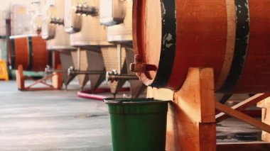 Bir fabrikadaki ahşap şarap fıçıları. Ağızdan küçük bir kovaya damlayan şaraplar. Yaşlanma sürecinde arka planda diğer variller ve metal tanklarla çevrili..