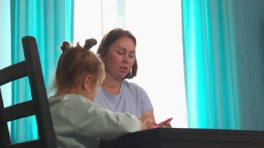 Kafkasyalı küçük kızın en alt görüntüsü annesiyle bir masada, parlak bir anaokulu ortamında kil şekillendiriyor. Aktivitelerdeki eller hayal gücünü, erken öğrenmeyi ve hassas motor koordinasyonu geliştirir..