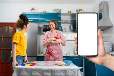 İki mutlu beyaz kadın mutfakta birlikte yemek pişiriyor. Bir kadının elinde akıllı bir telefon var. Model gibi. LGBT çiftleri ve aile yemekleri kavramı.